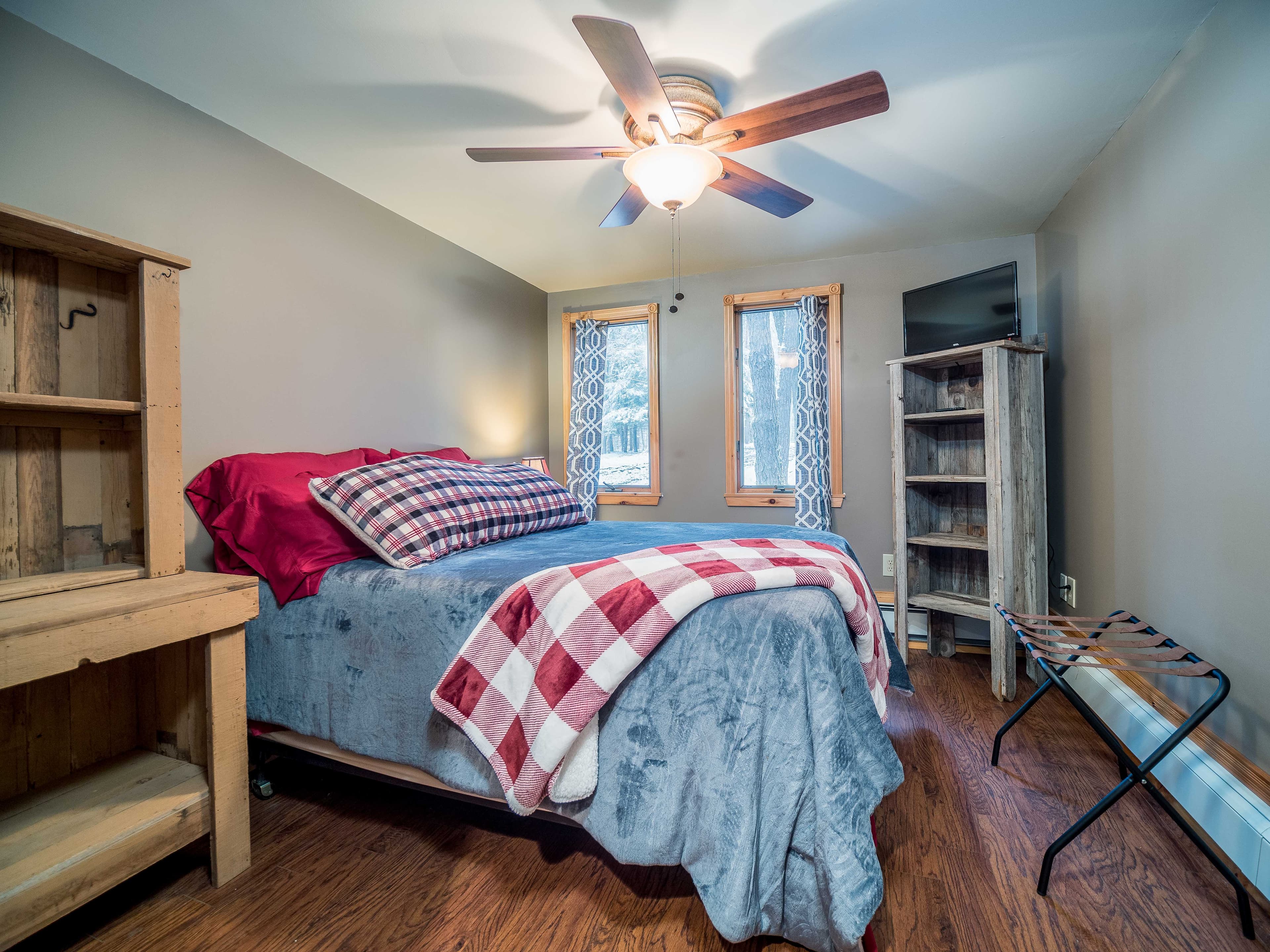 A first floor bedroom with plaid bedding, wood floors, and forest windows